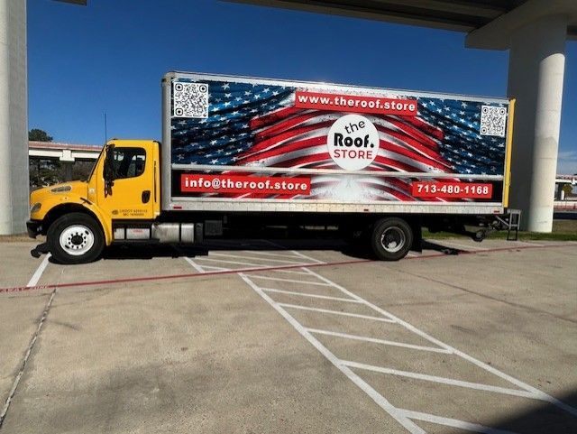 Yellow truck with a patriotic flag design on the side, parked in a concrete lot. 