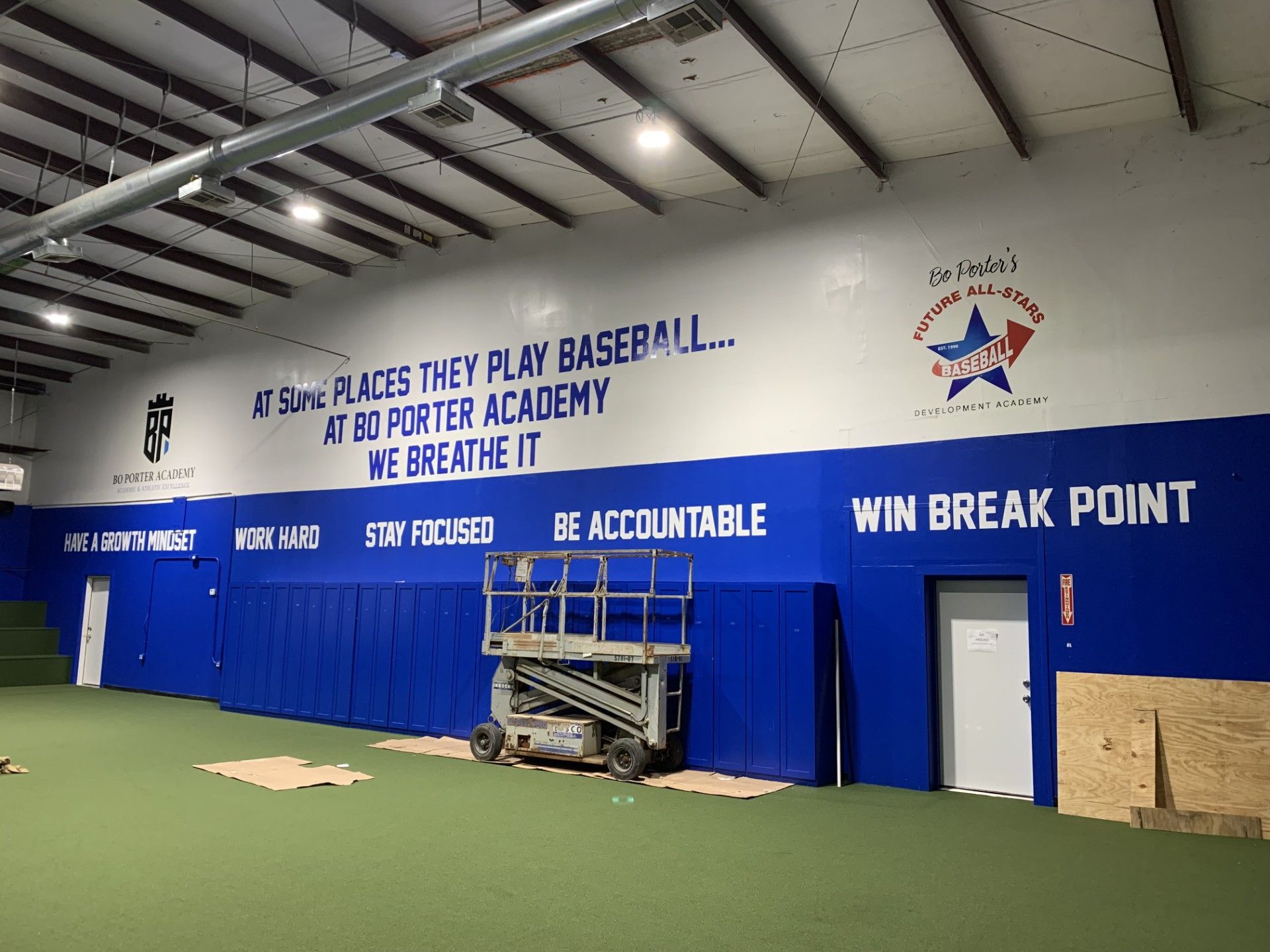 Interior of a baseball training facility with motivational quotes and team logos painted on a blue and white wall.