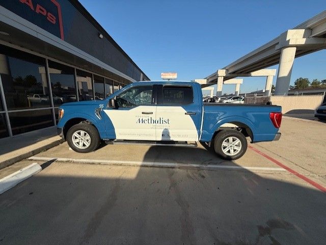 Blue and white Methodist truck parked in front of a building with a blue sky.