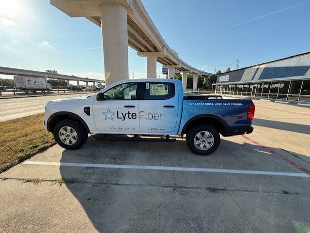 White and blue Lyte Fiber truck parked under a highway overpass on a sunny day.