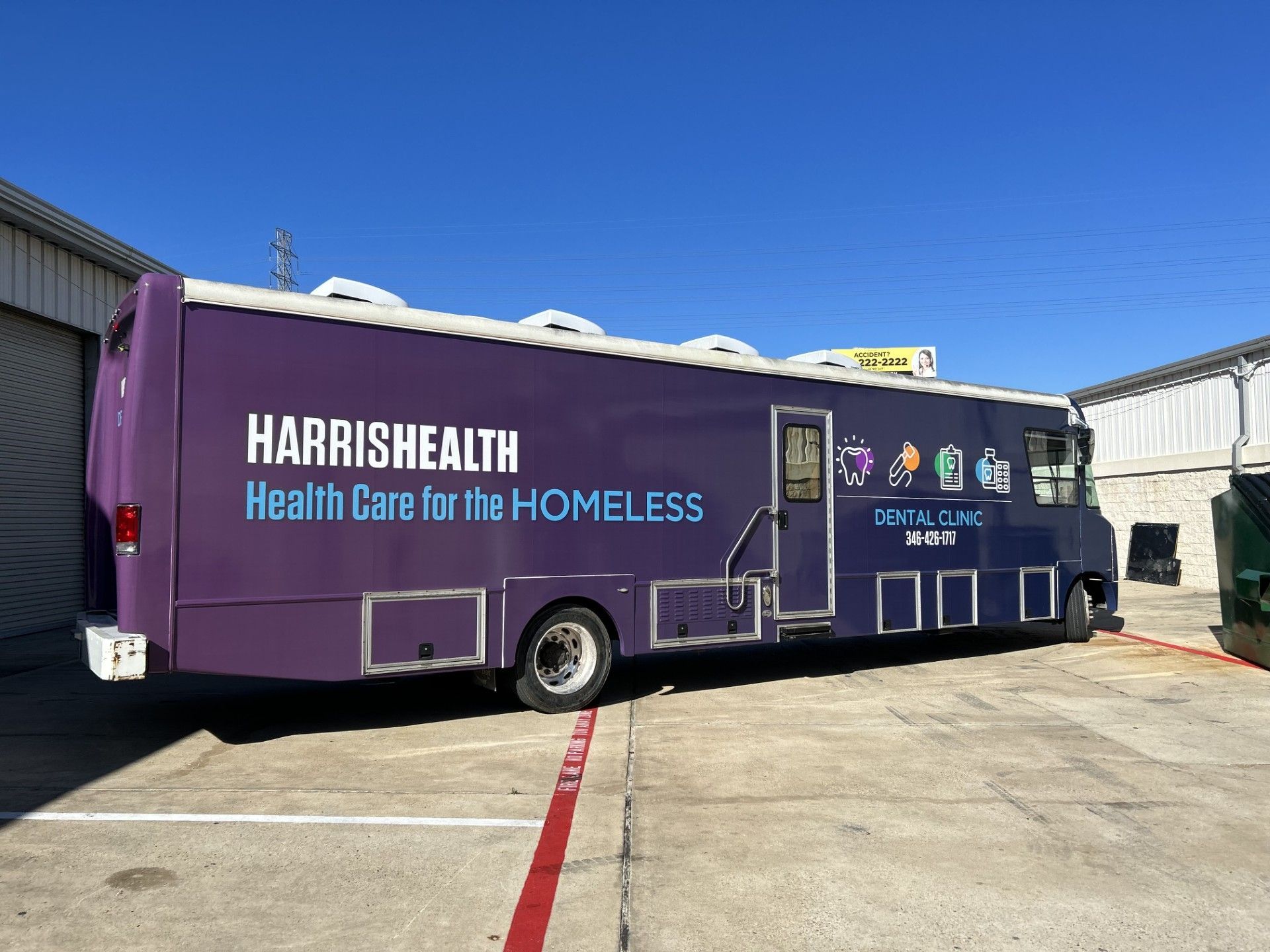Purple Harris Health mobile clinic providing healthcare for the homeless; parked outside under a blue sky.
