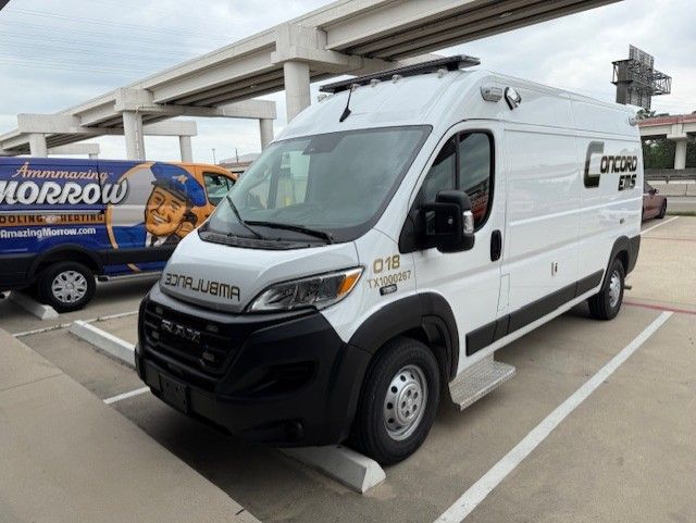 White emergency response van parked outdoors. The van has black accents and emergency lights on the roof. Another van is visible behind it.
