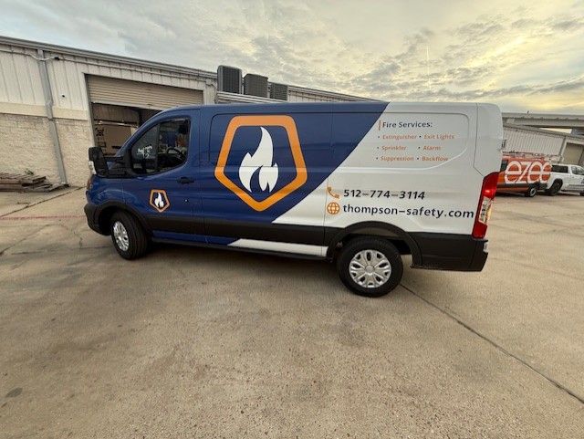 Blue and white service van with flame logo, parked outdoors. 