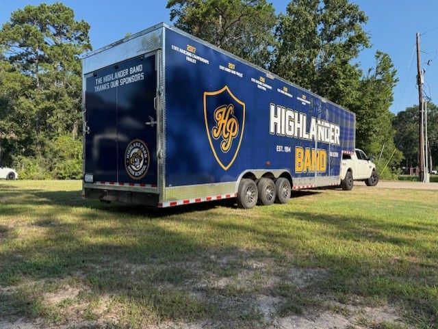 Blue Highlander Band trailer with truck on grassy area, sunny day.