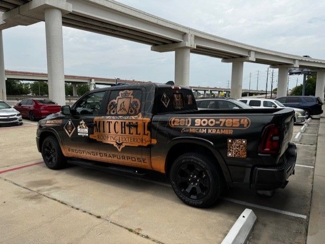 Black pickup truck with business graphics parked in a lot, under an overpass.