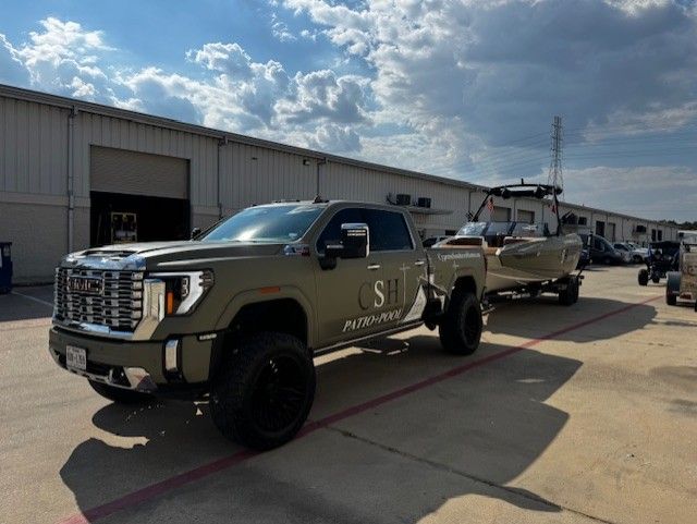 Olive green pickup truck towing a boat on a trailer, parked outside a building.
