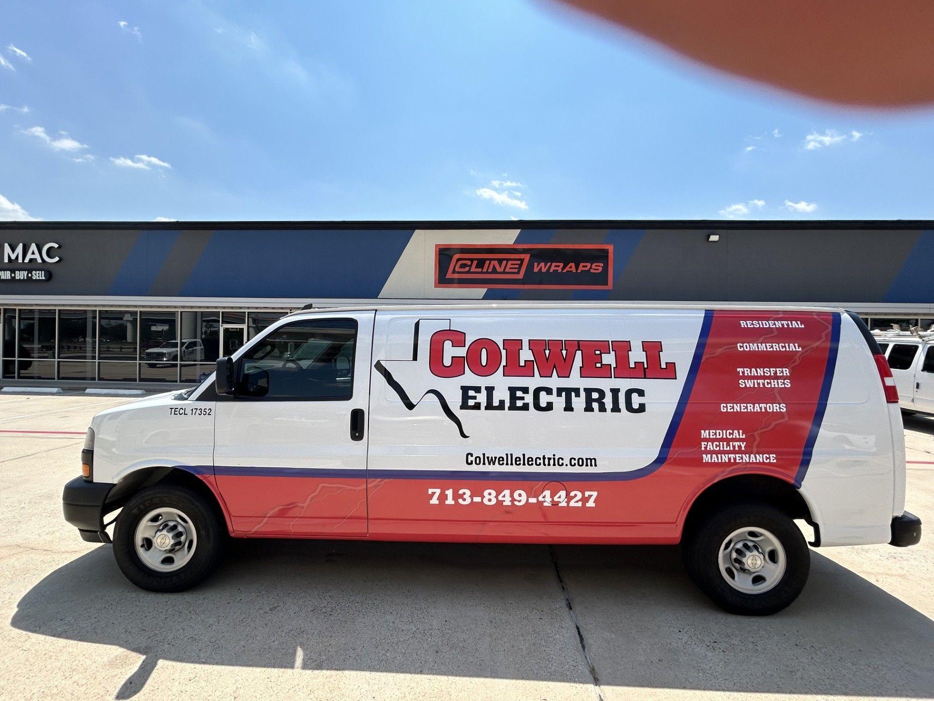 White and red Colwell Electric van parked in front of a building with a blue sky.
