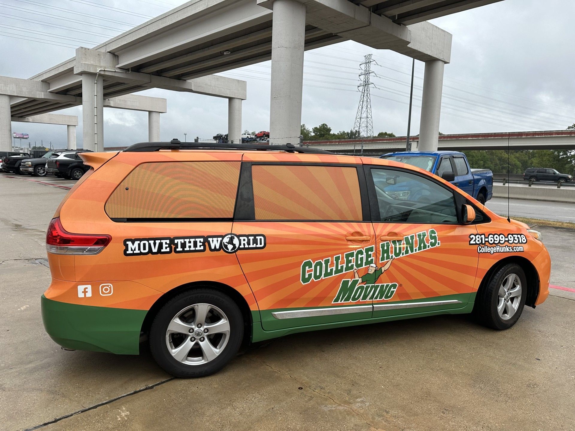 Orange and green College Hunks moving van under an overpass.