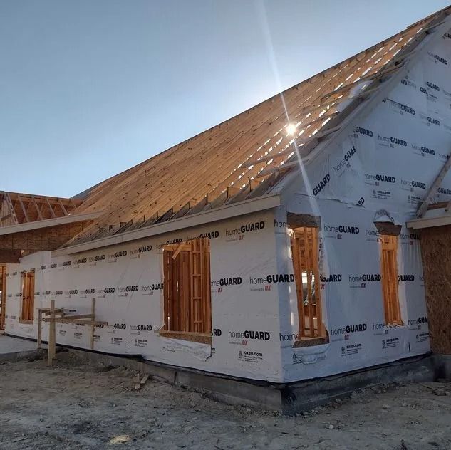 House under construction with wood framing, sheathing, and weather-resistant barrier, bright sunlight.