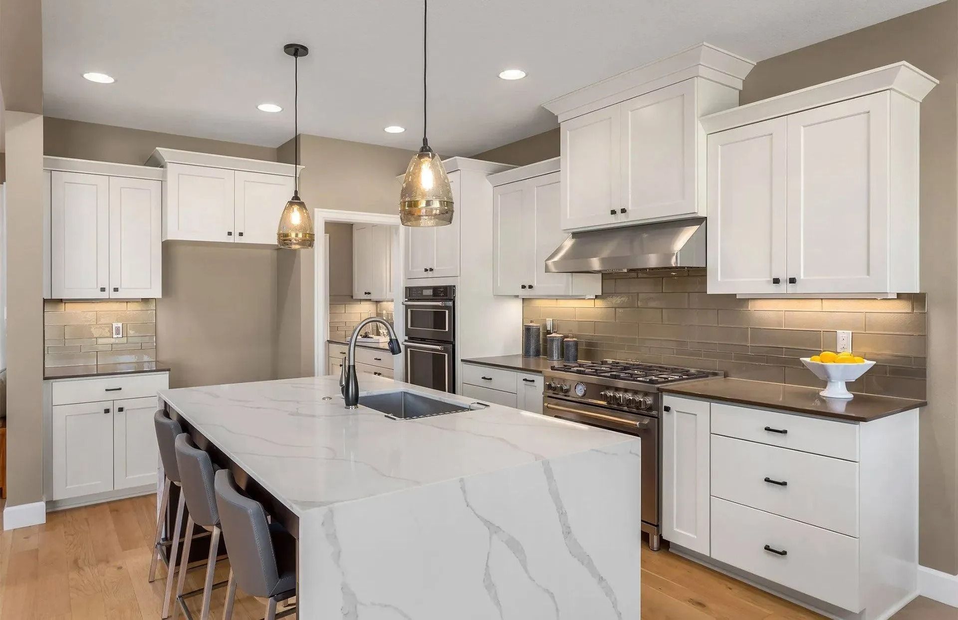 Modern kitchen with white cabinets, marble island, stainless steel appliances, and pendant lights.