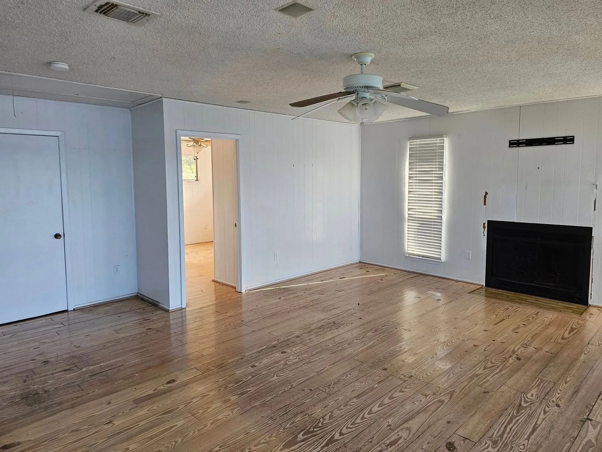 Empty living room with wood floors, white walls, and a black fireplace.