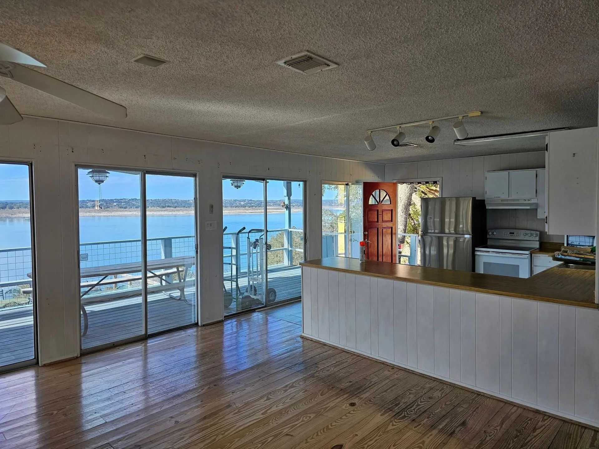 Bright living space with lake view, large windows, wood floor, white kitchen, and a red front door.