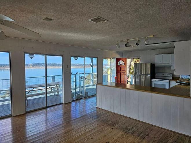 Bright living space with lake view, large windows, wood floor, white kitchen, and a red front door.