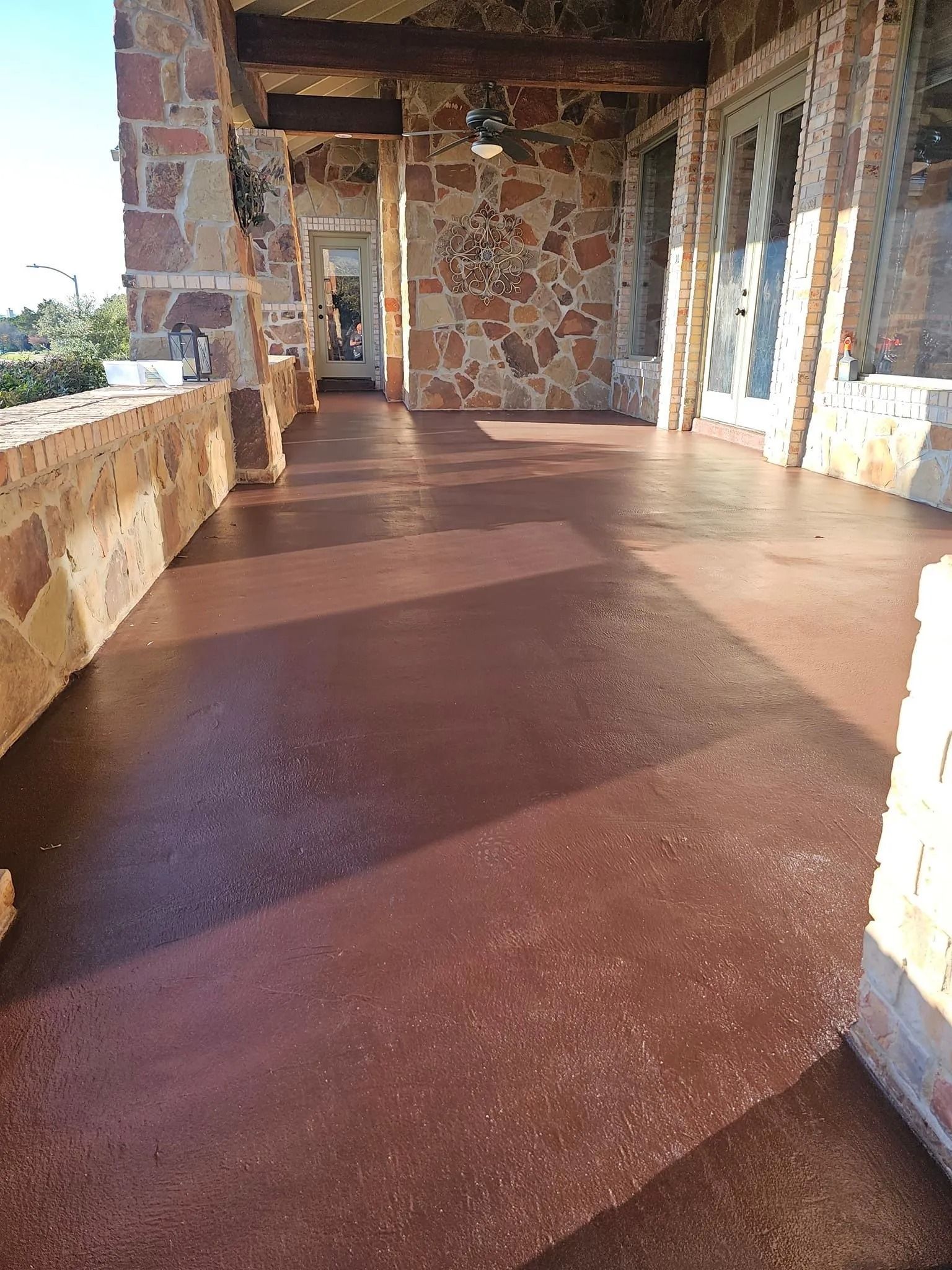 Brown-stained concrete patio with stone walls and columns. Sunlight casts shadows, illuminating the space.
