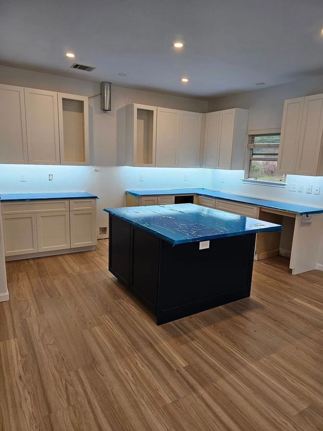 Kitchen renovation with white cabinets, blue countertops, dark island, and wood flooring.