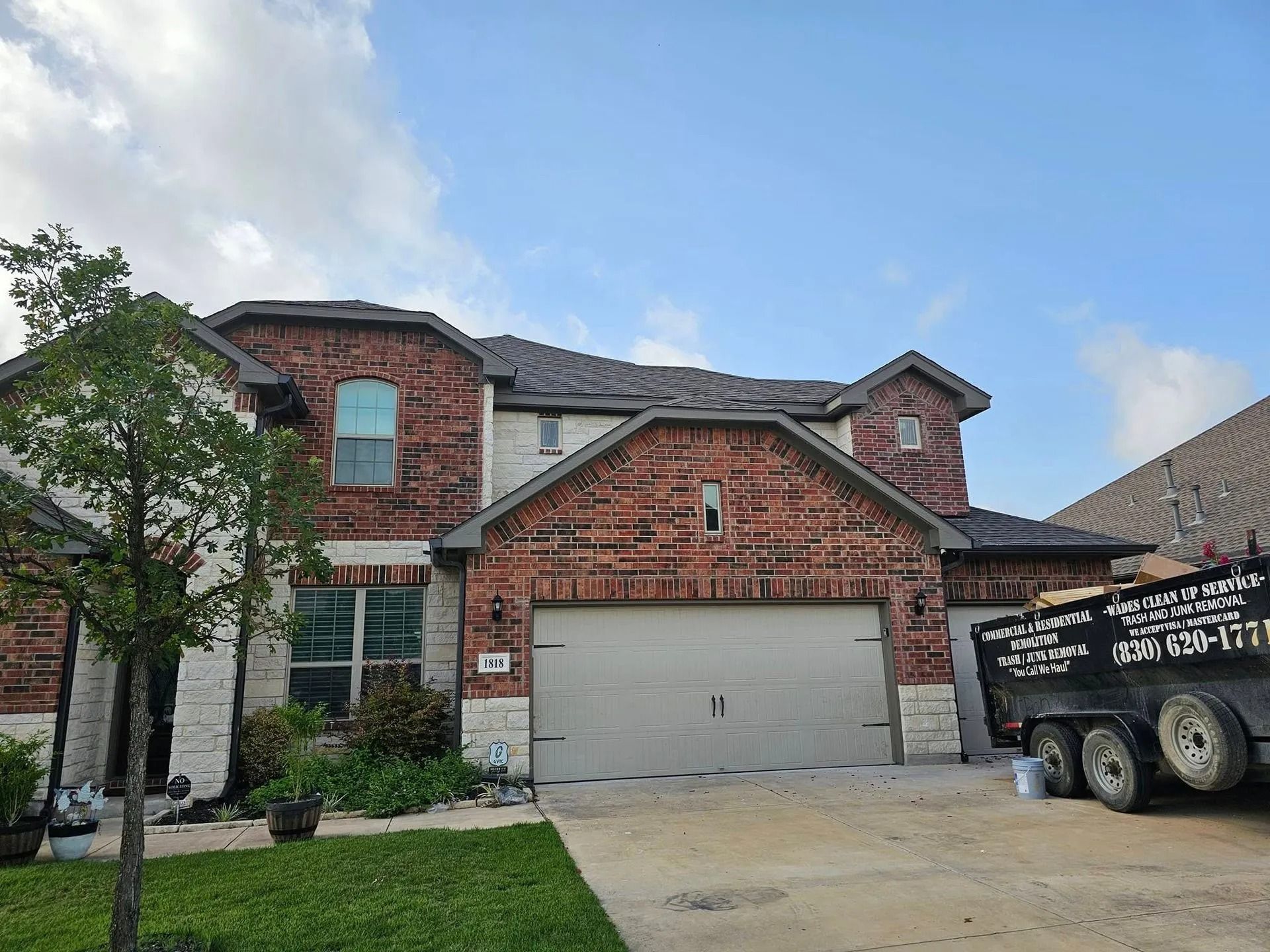 Two-story brick house with a garage and gray roof under a partly cloudy sky.