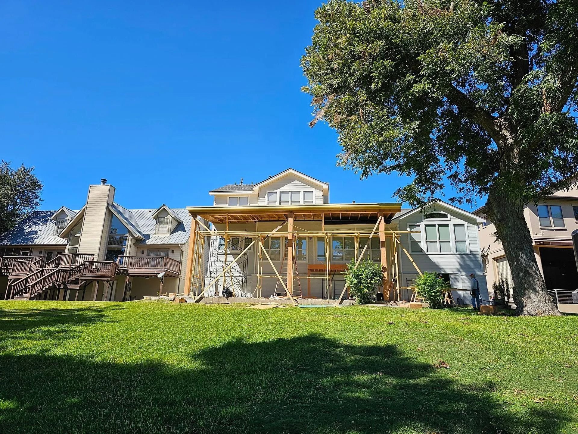 Backyard view of a house under construction with a wooden frame, sunny day. Green grass and blue sky.
