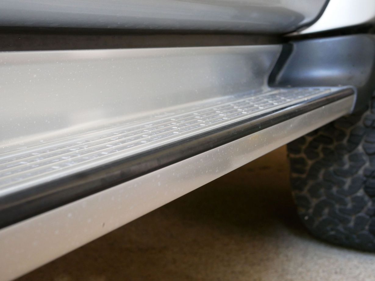 Close-up of a silver SUV’s running board and side step with textured tread near the rear wheel.