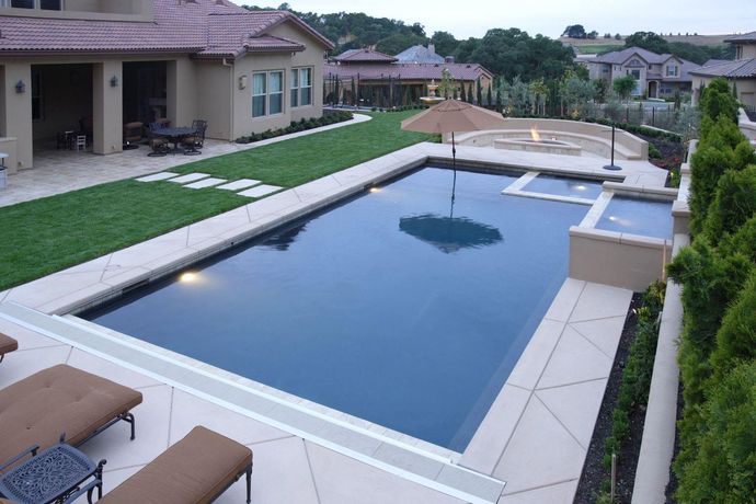 Luxury backyard pool lit at night beside a modern house and palm trees
