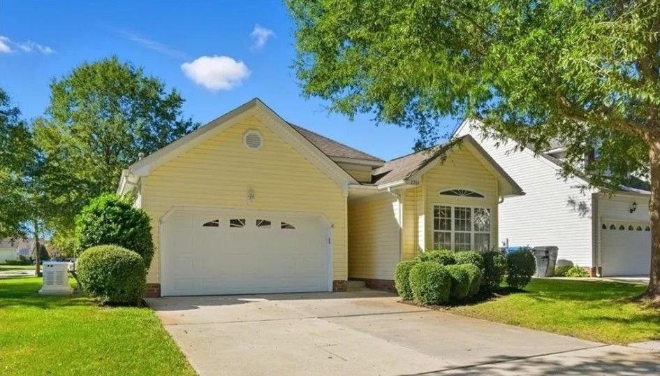 Yellow house with white garage door, blue sky, and green grass.