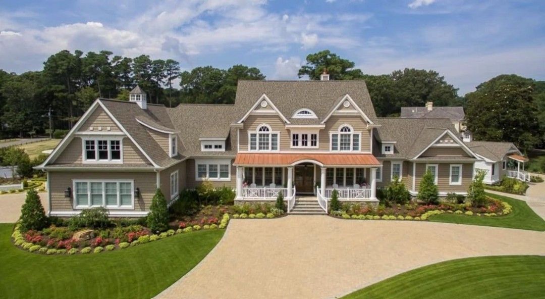 Large, beige multi-story house with a long driveway and well-manicured lawn.