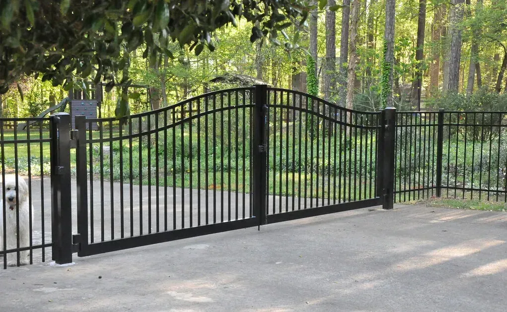 Black wrought iron gate on driveway, leading to a forested area.