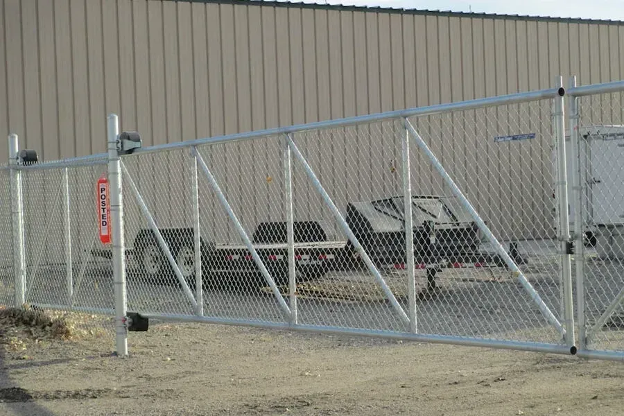 Chain-link gate, open, with white metal frame, in front of a building. A trailer sits behind the gate.