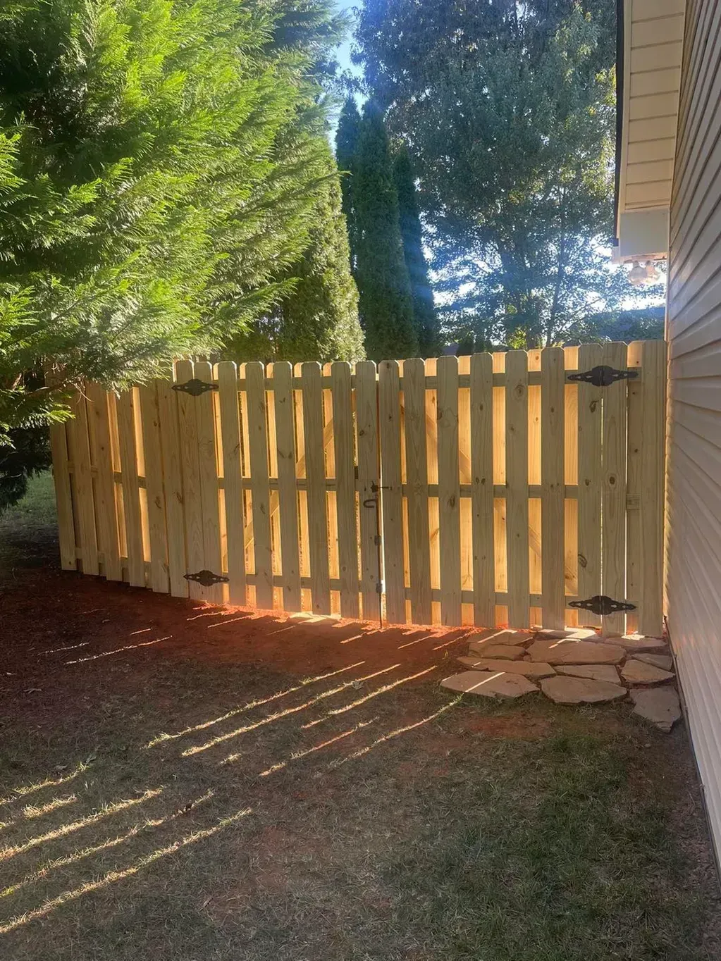 A wooden fence with two gates on a sunny day, next to a house.