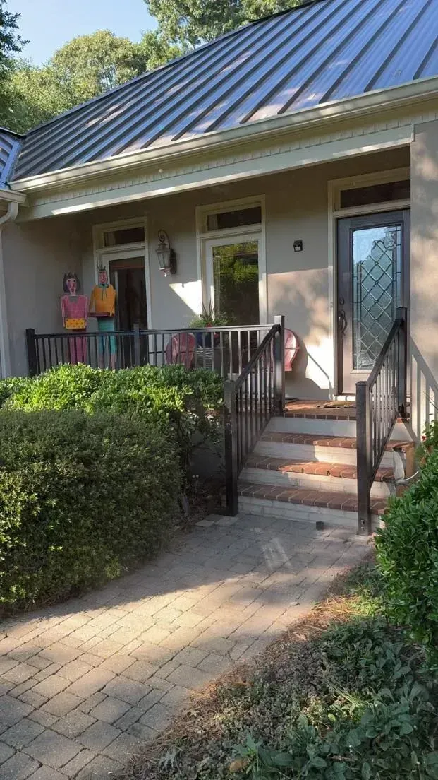 Small house with porch. People standing on porch, brick pathway.