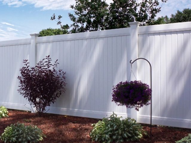 White vinyl fence with hanging flower basket and purple flowering bushes.