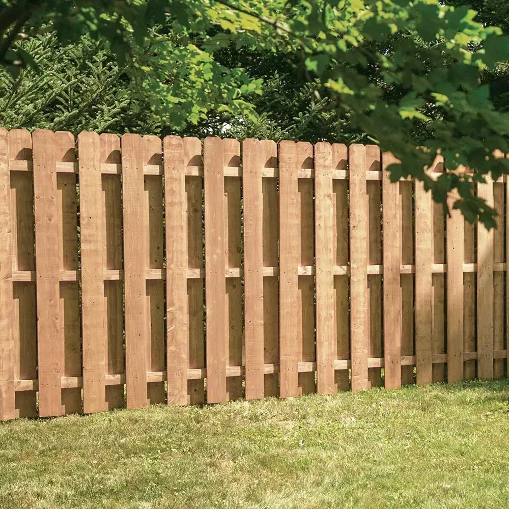 Wooden fence in a grassy yard with green trees in the background.