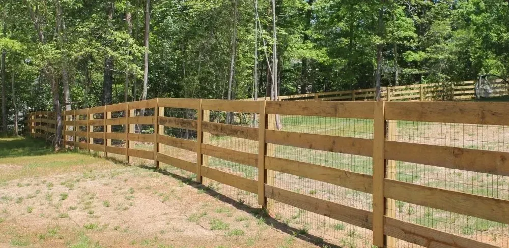 Wooden fence in a field with trees in the background.