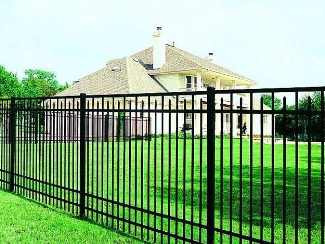Black metal fence surrounding a green yard, with a beige house in the background.