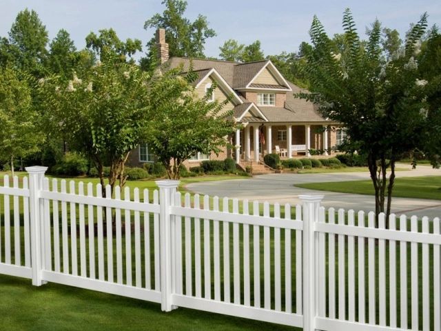 White picket fence in front of a large house with trees and green lawn.