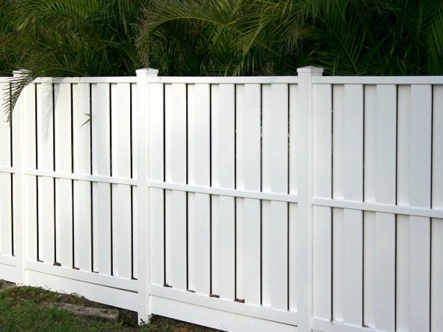 White vertical plank fence with green foliage backdrop.