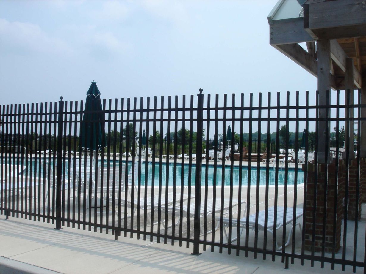 Black metal fence in front of a house with a light-colored exterior and a green lawn.