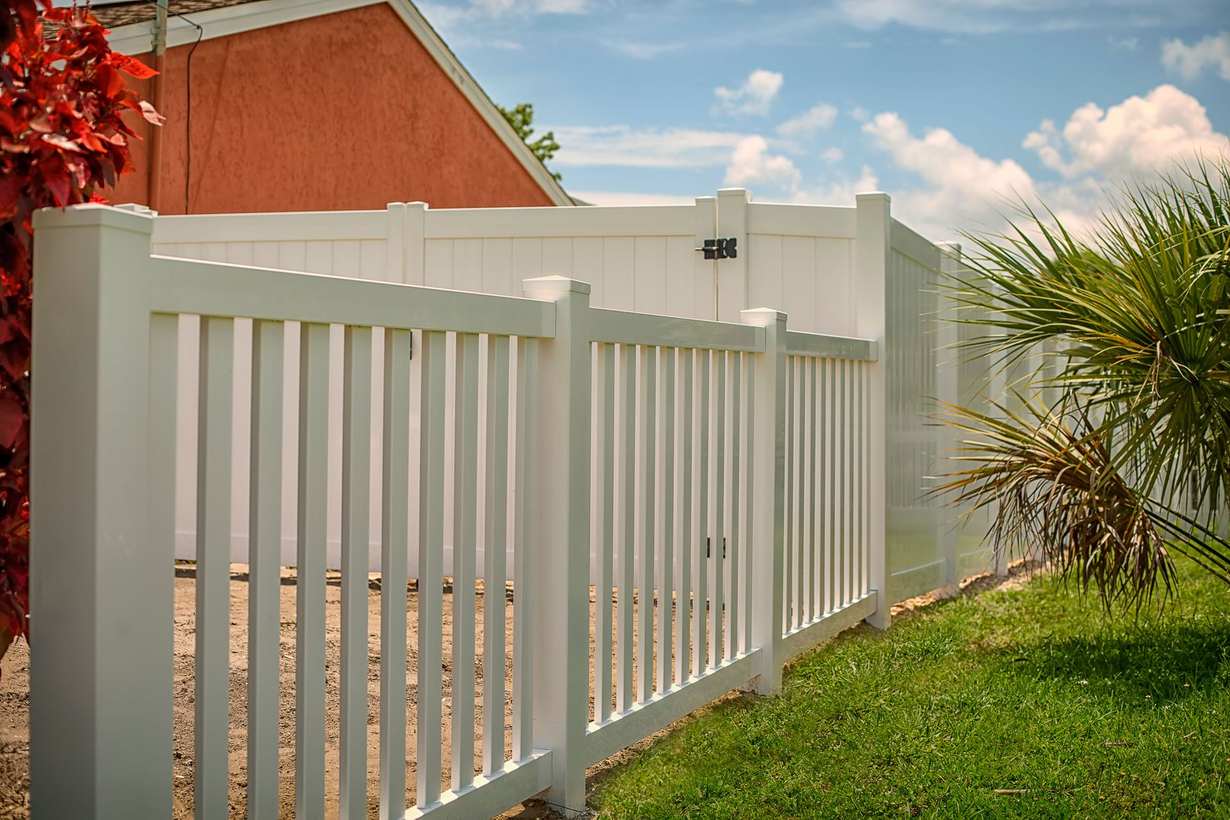 White vinyl privacy fence with vertical slats, in front of green foliage.