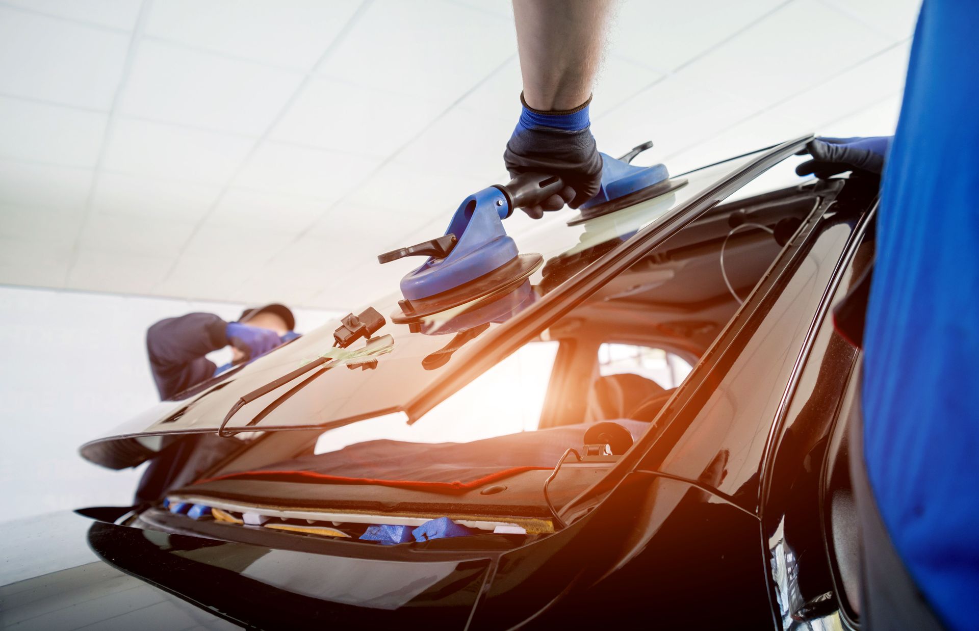 Car windshield being replaced by a mechanic using suction cup tools in a garage.