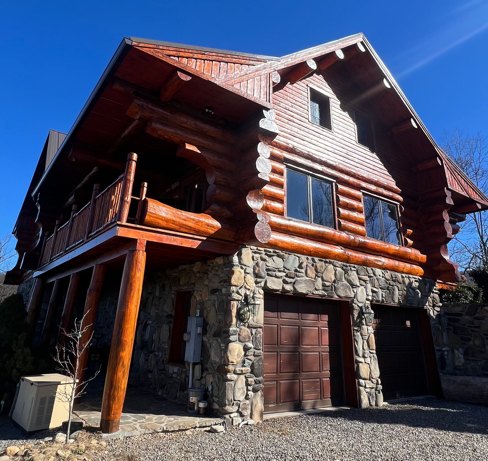 Log cabin with wooden exterior and stone base, garage doors, and blue sky.