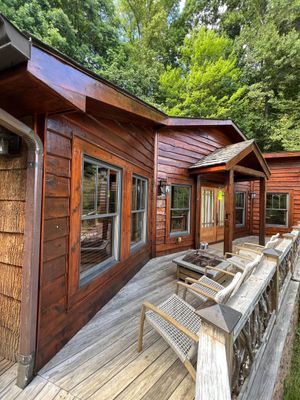 Wooden cabin with deck and windows, surrounded by trees.