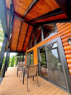 Wooden cabin porch with seating, overlooking green trees.