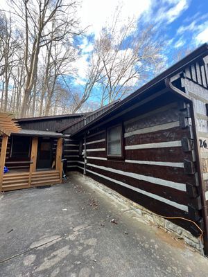 Log cabin with dark brown logs and light chinking. The roof is brown, set in a wooded area.