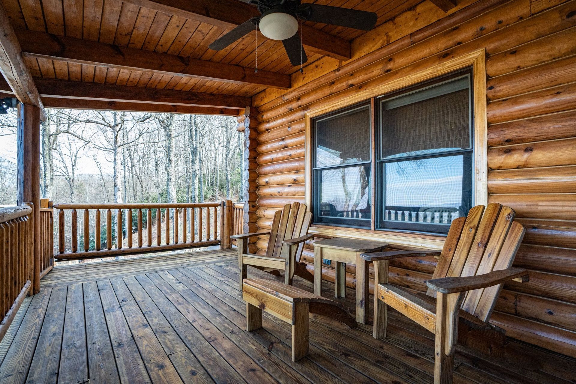Wooden porch with two chairs, a small table, and a view of trees through a window.