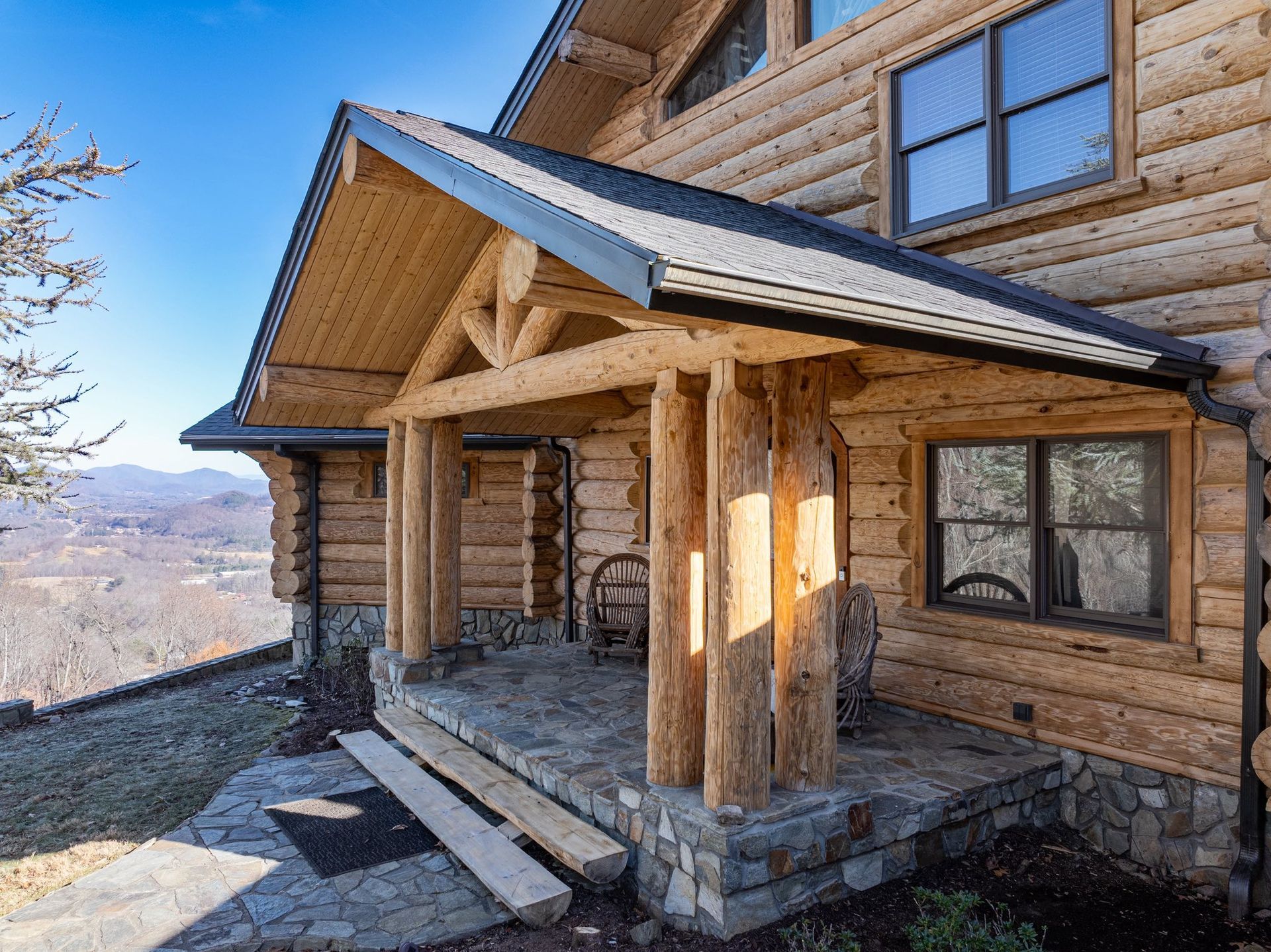 Log cabin with a covered porch overlooking a mountain vista.