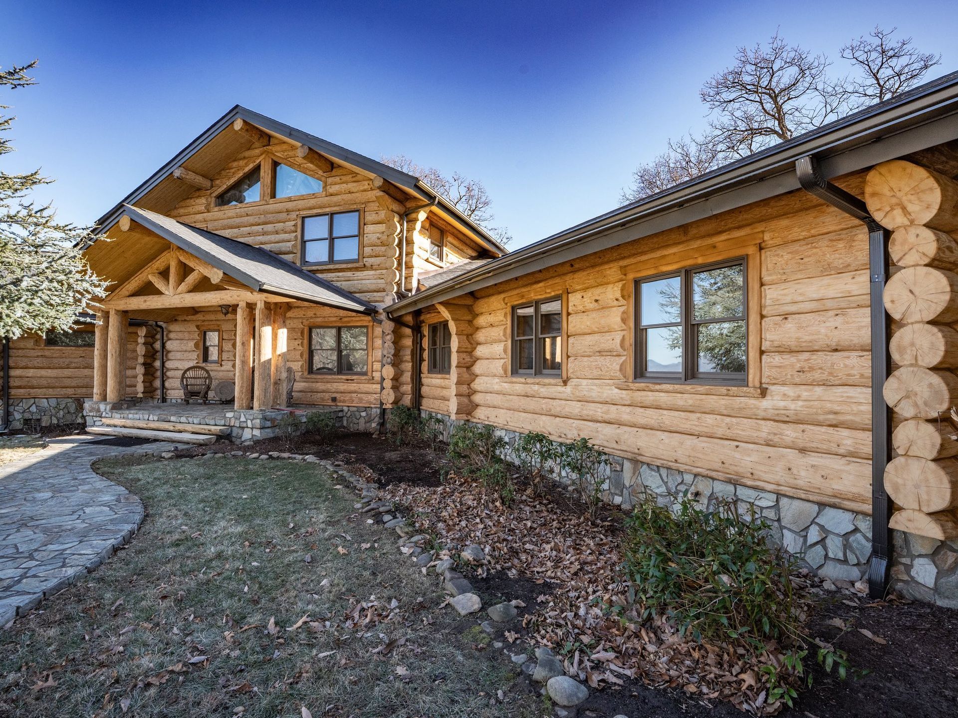 Wooden log cabin house with a porch and landscaping under a clear sky.
