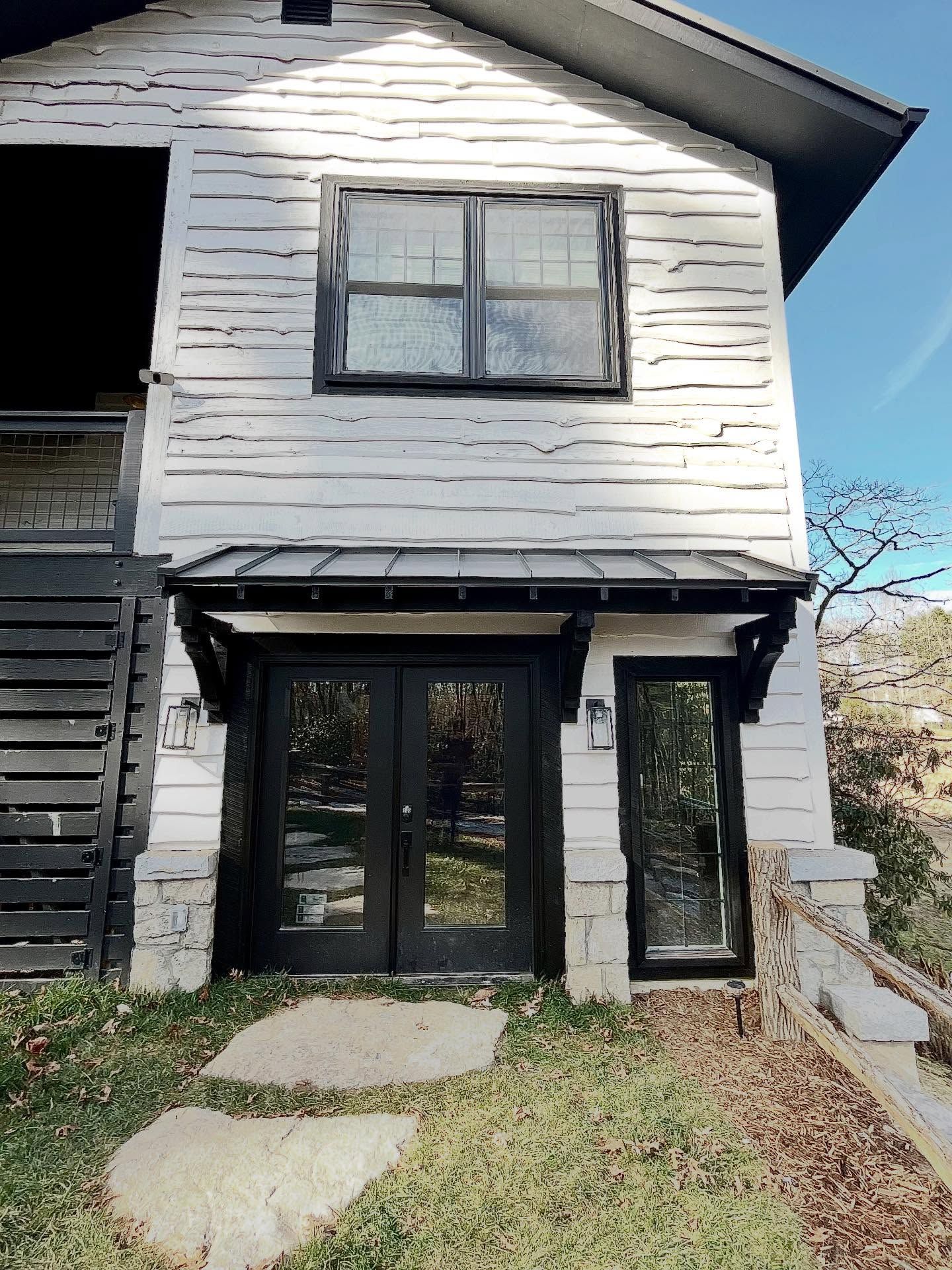 White, weathered building with black door and windows, awning. Stone pathway leading to entrance.