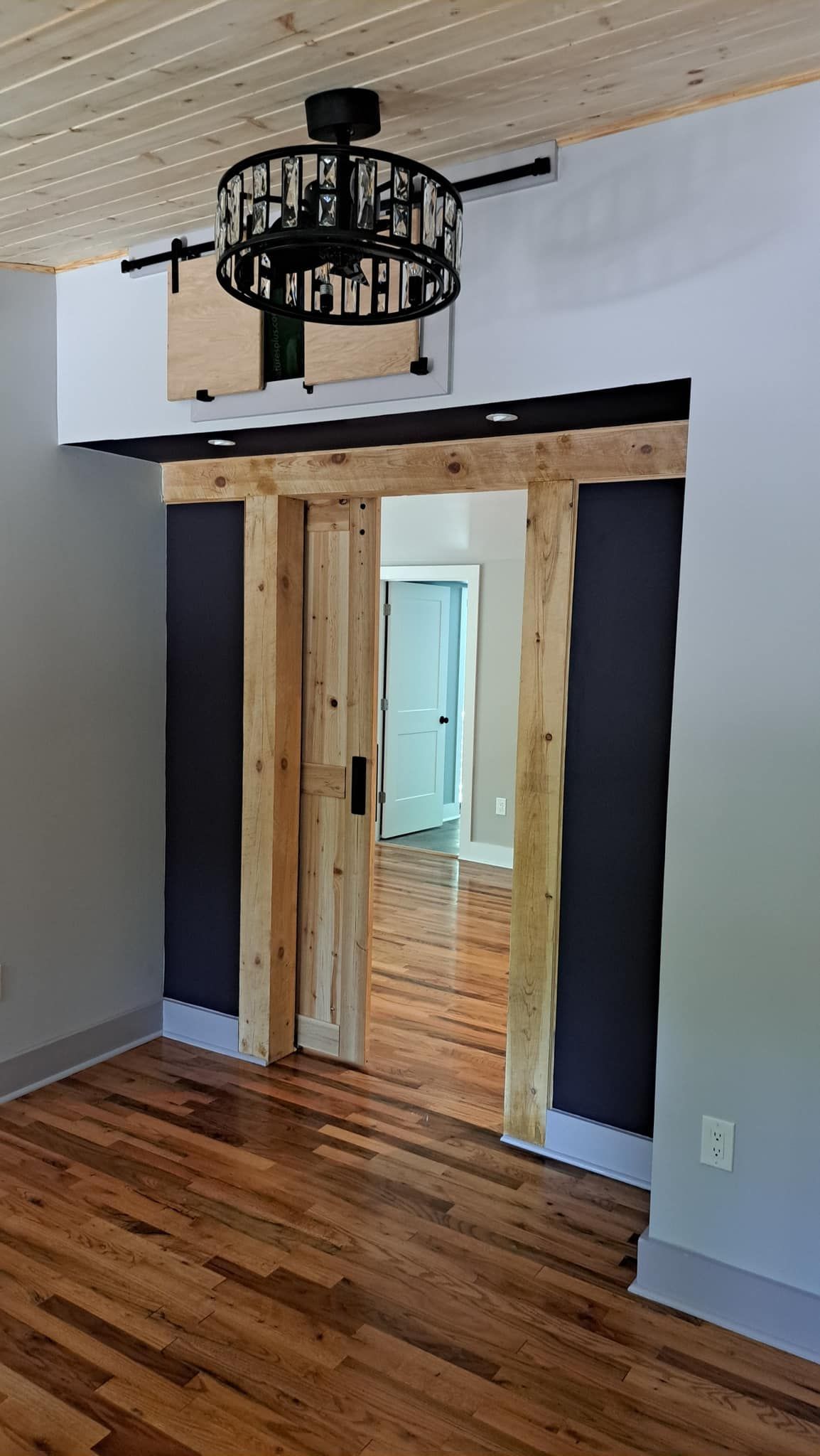 Wooden sliding door in a room with hardwood floors and a decorative light fixture.