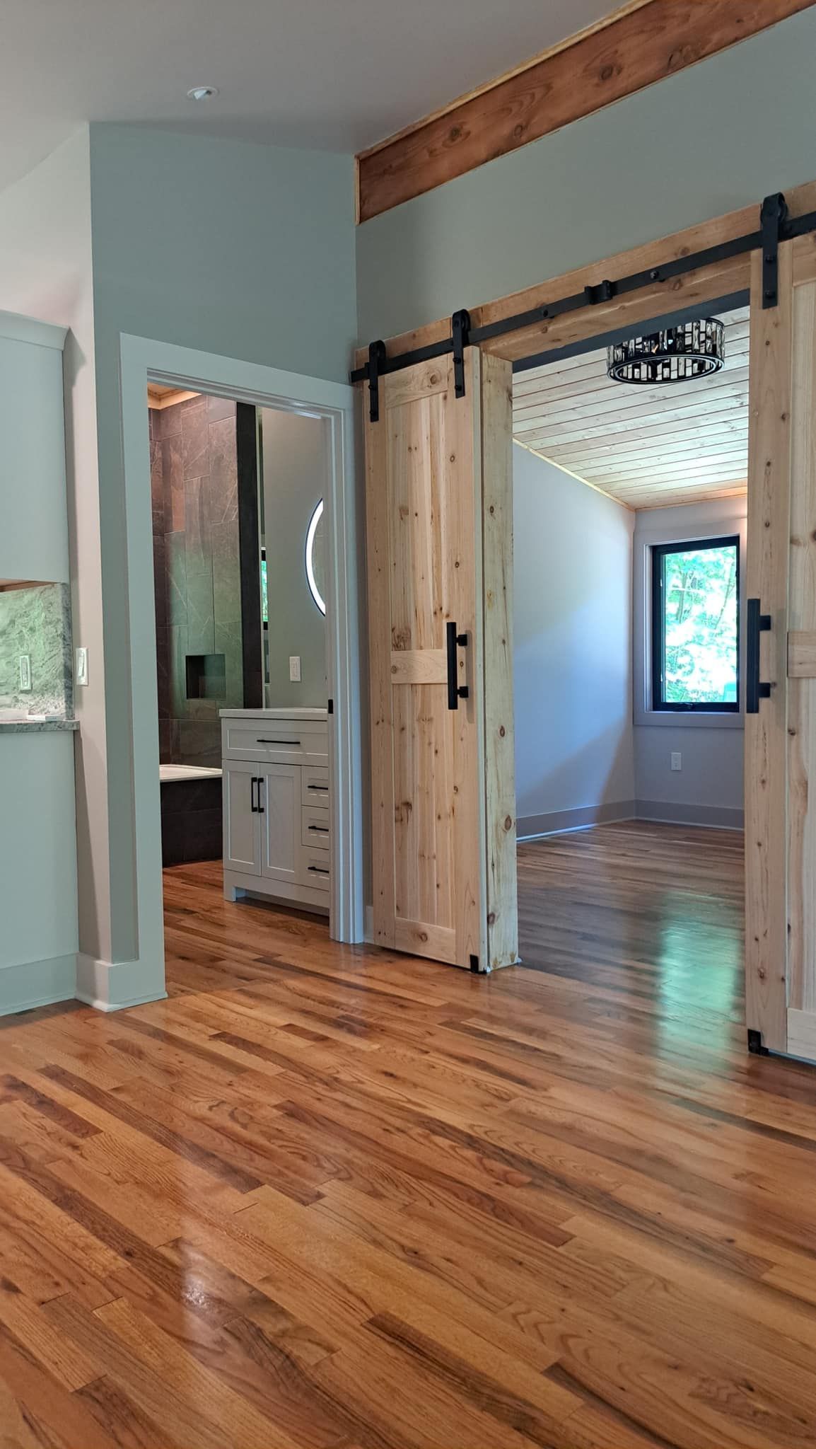 Wooden barn doors open to reveal a room with a decorative ceiling. Bathroom with blue wall is on the left.