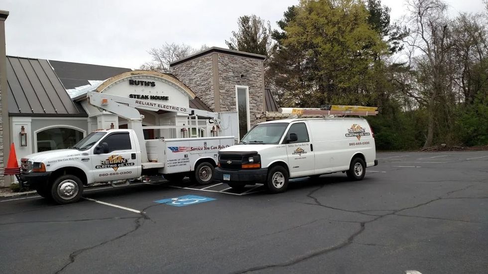 Two work trucks parked in front of a building. One white truck with the logo
