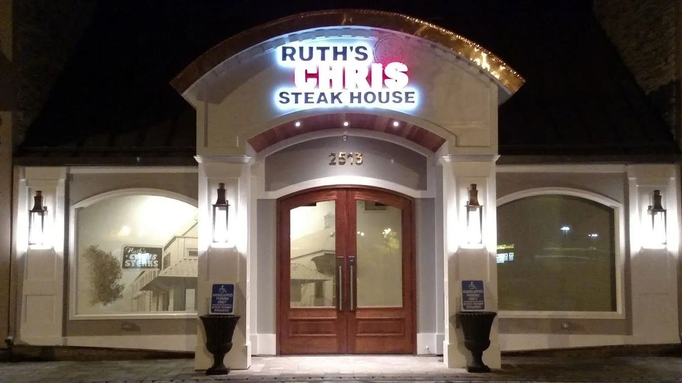 Ruth's Chris Steak House entrance at night with illuminated sign and lights. Brown double doors.